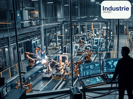 Industrielle Fertigungshalle mit mehreren Industrierobotern und einem Bediener vor mehreren Monitoren mit digitalen Anzeigen