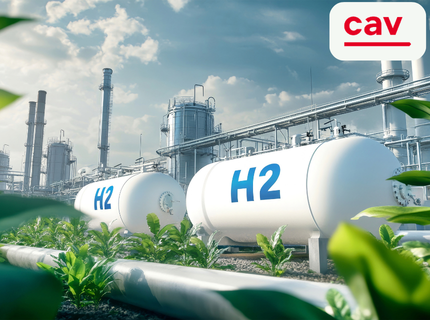 Zwei große weiße Wasserstofftanks mit der Aufschrift 'H2' in einer Industrieanlage mit Rohrleitungen und grünem Pflanzenbewuchs im Vordergrund